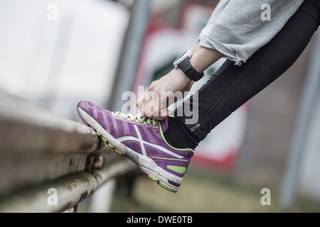 Sezione bassa di donna laccio di legatura della calzatura sportiva su parapetto Foto Stock