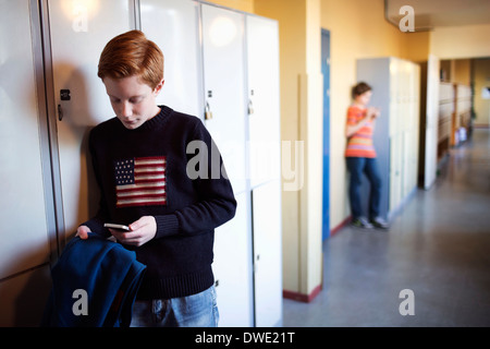 Studente di scuola superiore utilizzando il telefono cellulare da locker Foto Stock