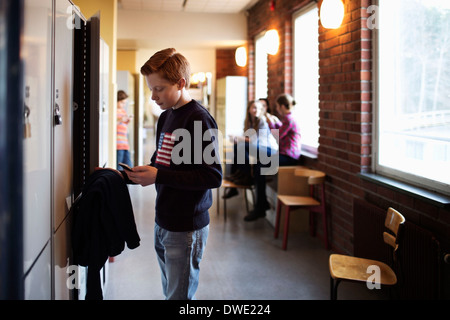 High school boy utilizzando il telefono cellulare da locker Foto Stock