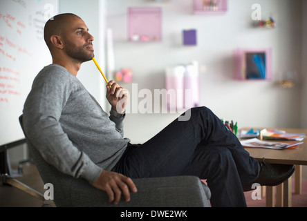 Imprenditore pensieroso seduto su una sedia in ufficio creativo Foto Stock