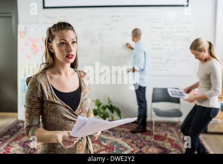 Imprenditrice azienda documenti mentre i colleghi che lavorano in background in ufficio Foto Stock