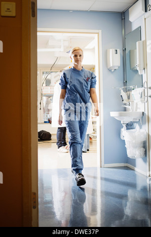 Per tutta la lunghezza della giovane donna infermiera camminando nel corridoio di ospedale Foto Stock