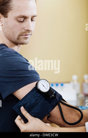 Medico mettendo un bracciale per la misurazione della pressione maschio sul braccio del paziente in clinica Foto Stock