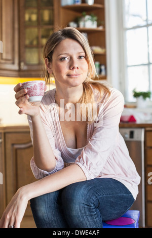 Ritratto di donna azienda tazza da caffè in cucina Foto Stock