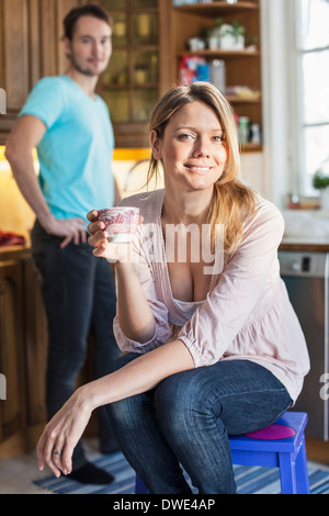 Ritratto di donna azienda tazza da caffè con uomo in background in cucina Foto Stock