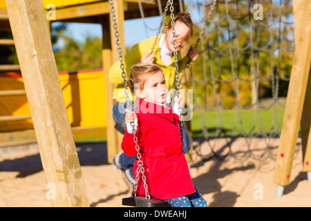 Famiglia con mamma e figlia basculante e giocare su area giochi o corte Foto Stock