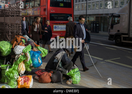 Come i passanti a piedi da, un senzatetto si siede con tutti i suoi averi su Piccadilly nel centro di Londra. Foto Stock