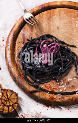 Spaghetti al nero (la pasta con il nero di seppia) con il polipo marinato e aglio grigliato servito sul tagliere di legno.