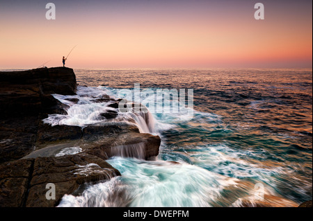 Un pescatore solitario sorge la pesca al tramonto Foto Stock