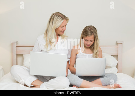 Madre e figlia utilizzando computer portatili a letto Foto Stock