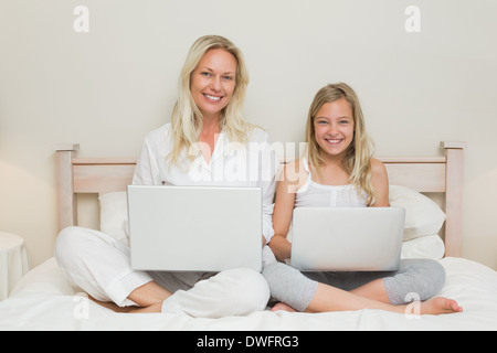 Felice madre e figlia utilizzando computer portatili a letto Foto Stock