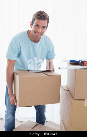 Uomo sorridente con scatole di cartone in casa nuova Foto Stock