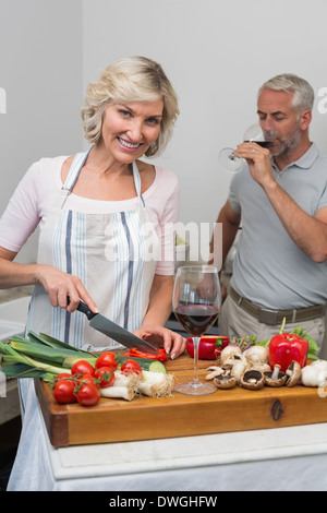 Uomo maturo con bicchiere di vino e la donna tritare verdure in cucina Foto Stock