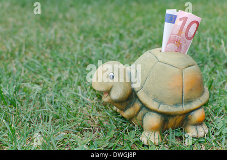 Tartaruga felice Salvadanaio con dieci di banconote in euro nell'erba verde Foto Stock