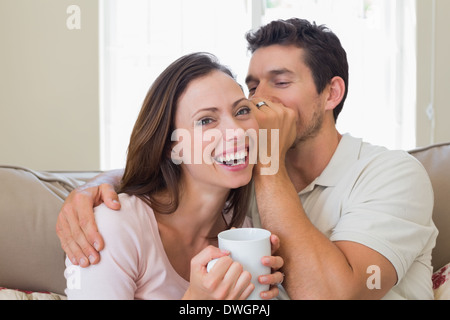 L'uomo whispering segreto in un allegro womans orecchio in salotto Foto Stock