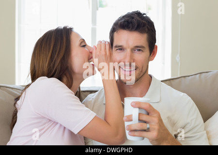 Donna sussurro segreto in un felice mans orecchio in salotto Foto Stock