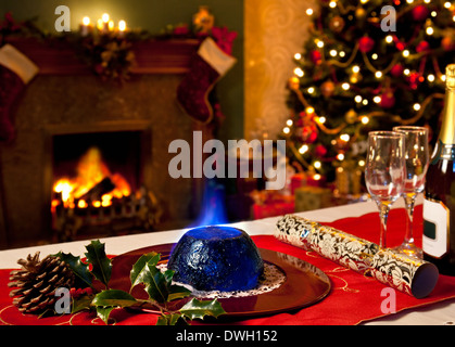 Un pudding natalizio con ardente brandy topping con un festoso sullo sfondo di un camino e un albero di Natale. Foto Stock