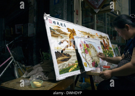 Una donna sta lavorando su un arti e mestieri progetto presso il suo negozio fino a tarda notte su una strada di città in Kampong Cham, Cambogia. Foto Stock