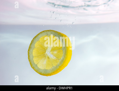 Spicchi di limone a cadere attraverso l'acqua contro uno sfondo bianco Foto Stock