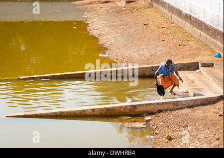 L' India , il Tamil Nadu , Chettinad , Karakaikudi , vecchio uomo maschio wok pulisce brasiera utensile nel tempio della piscina di acqua bassa quasi vuota Foto Stock