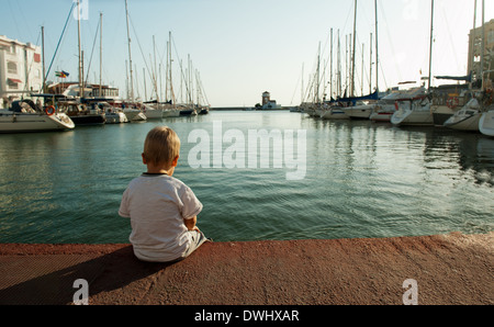 Piccolo Ragazzo seduto da solo nel porto Foto Stock