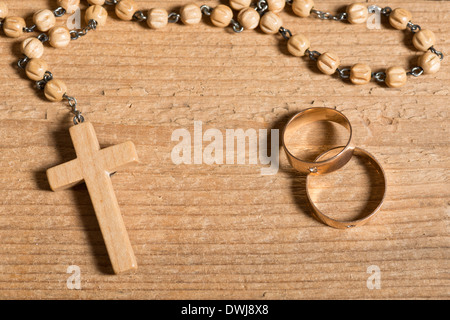 Gli anelli di nozze e rosario sulla vecchia scrivania in legno Foto Stock