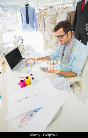 Designer di moda utilizzando notebook e cellulare Foto Stock