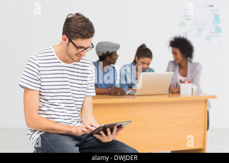 Artista con tavoletta digitale con i colleghi in background in ufficio Foto Stock