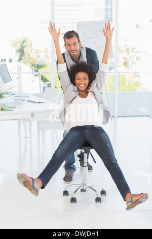 Giocoso giovane donna di spinta sulla sedia in ufficio Foto Stock