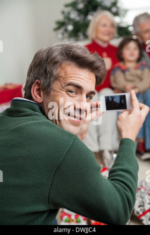 Padre fotografare la famiglia tramite smartphone Foto Stock