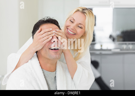 Donna sorridente felice di copertura mans agli occhi in cucina Foto Stock