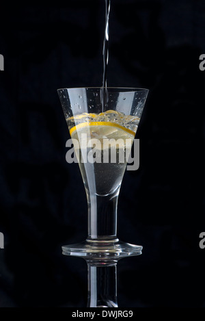 L'acqua versata in un bicchiere con una fettina di limone Foto Stock