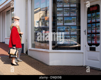 Coppia di anziani in cerca nella finestra di un agente immobiliare, Bude, Cornwall, Regno Unito Foto Stock