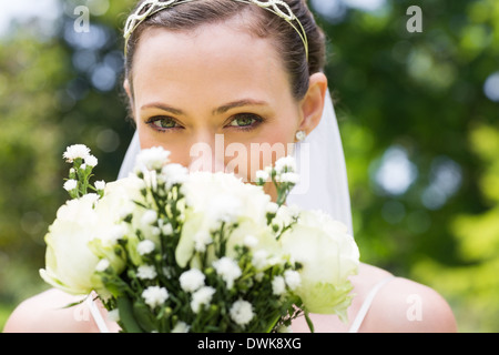 Sposa peeking oltre il mazzo di fiori in giardino Foto Stock