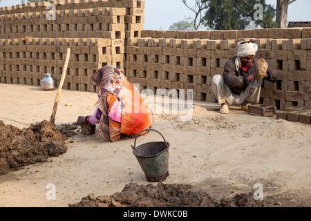 Rajasthan, India. Moglie prepara il fango morbido mentre mio marito lo mette in stampi per mattoni. Foto Stock