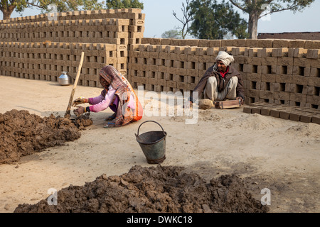 Rajasthan, India. Moglie prepara il fango morbido mentre mio marito lo mette in stampi per mattoni. Foto Stock