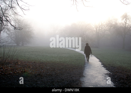 Donna anziana su sentiero nella nebbia meteo, Priory Park, Warwick, Regno Unito Foto Stock