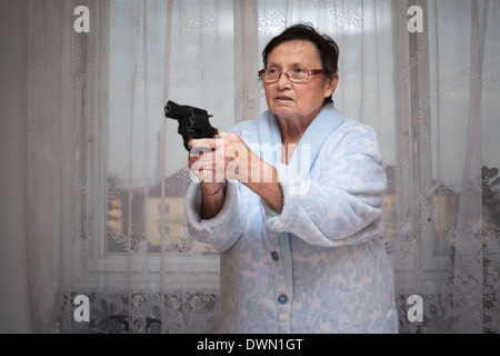 Spaventata senior donna puntando una pistola in ambienti chiusi. Foto Stock