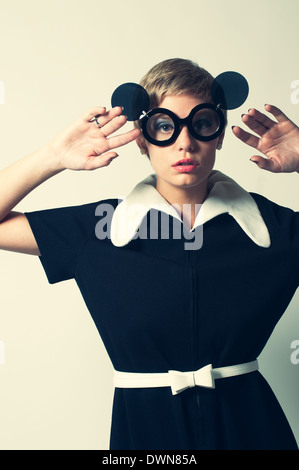 Una donna retrò in posa di un mod 60s abito, posa con flip up occhiali da sole rotondi, in alto le mani, un retro 60s di moda vintage concept Foto Stock