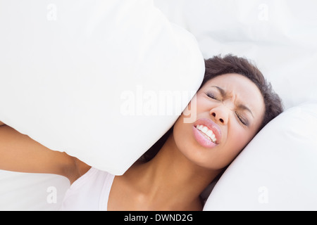 Ha sottolineato bruna seduta sul letto che copre le orecchie con cuscino Foto Stock