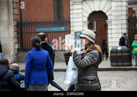 Donna che utilizza dispositivo Tablet guardare gli artisti interpreti o esecutori sul mercato di Covent Garden Foto Stock