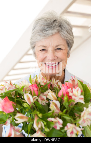 Donna in pensione tenendo bouquet di fiori sorridenti in telecamera Foto Stock