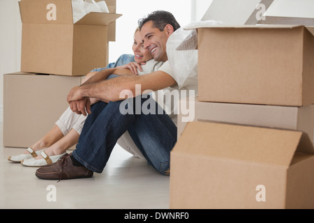 Sorridente giovane seduto in mezzo alle caselle nella nuova casa Foto Stock