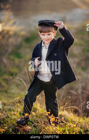 Carino piccolo ragazzo nel mantello e cappuccio sorridente nel campo di sera Foto Stock