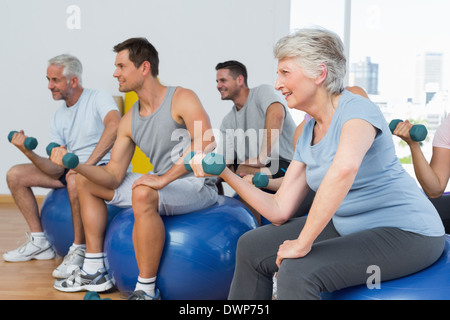 Classe con manubri seduti su palle ginniche in palestra Foto Stock