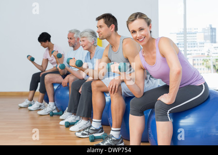 Classe con manubri seduti su palle ginniche in palestra Foto Stock