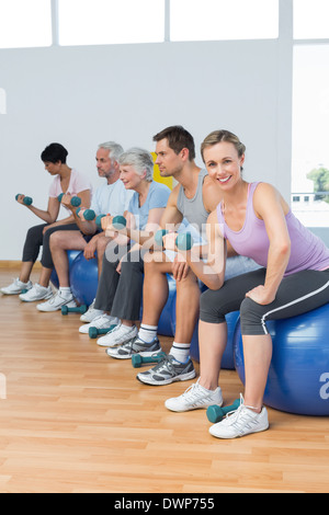 Classe con manubri seduti su palle ginniche in palestra Foto Stock