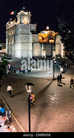 Scena di notte guardando verso il basso sulla Zocalo con vista del duomo illuminato & plaza con bambini che giocano la gente socializzare Oaxaca Foto Stock