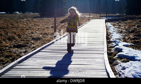 Ragazza che corre lungo la decking in legno pathway Foto Stock