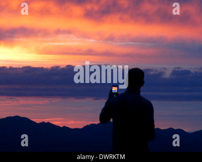 Un uomo prende una fotografia di un tramonto sul suo telefono cellulare. Foto Stock